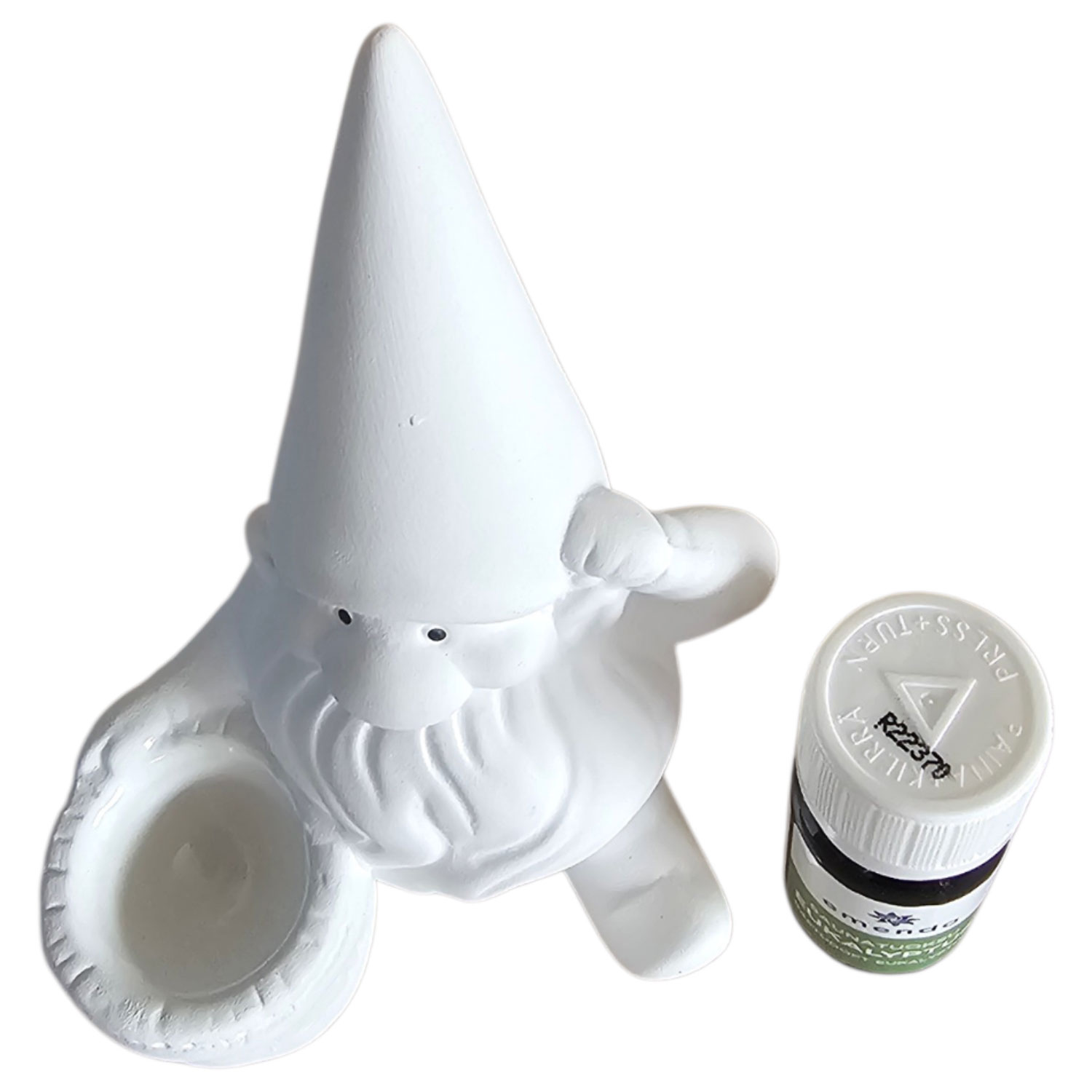Ein weißer Gartenzwerg-Kerzenhalter aus Keramik neben einer kleinen Flasche ätherischem Öl.