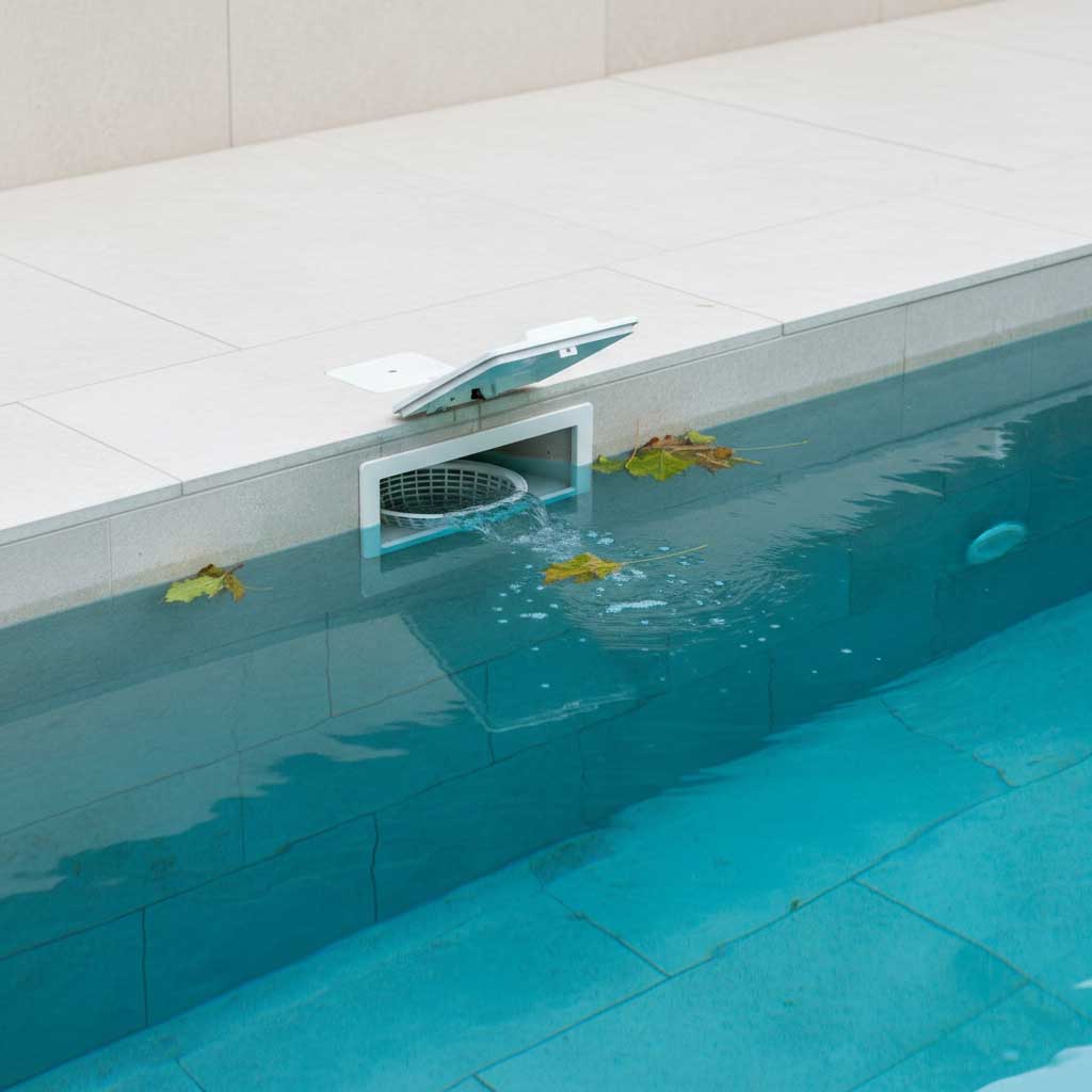 Nahaufnahme eines rechteckigen Skimmers in einem Schwimmbad mit offenem Deckel und Filterkorb.