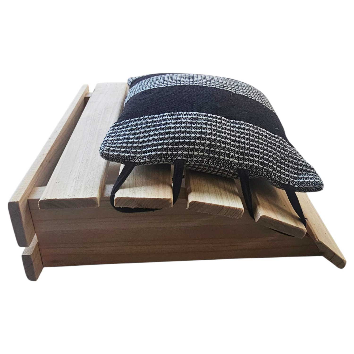Eine Sauna-Kopfstütze aus Holz mit einem daran befestigten schwarz-weiß gestreiften Stoffkissen.